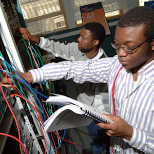 Two students looking at a textbook in front of a computer server Two students looking at a textbook in front of a computer server