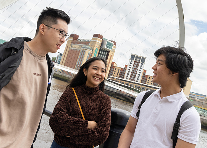 ثلاثة من طلاب نيوكاسل يقفون أمام نهر للدردشة