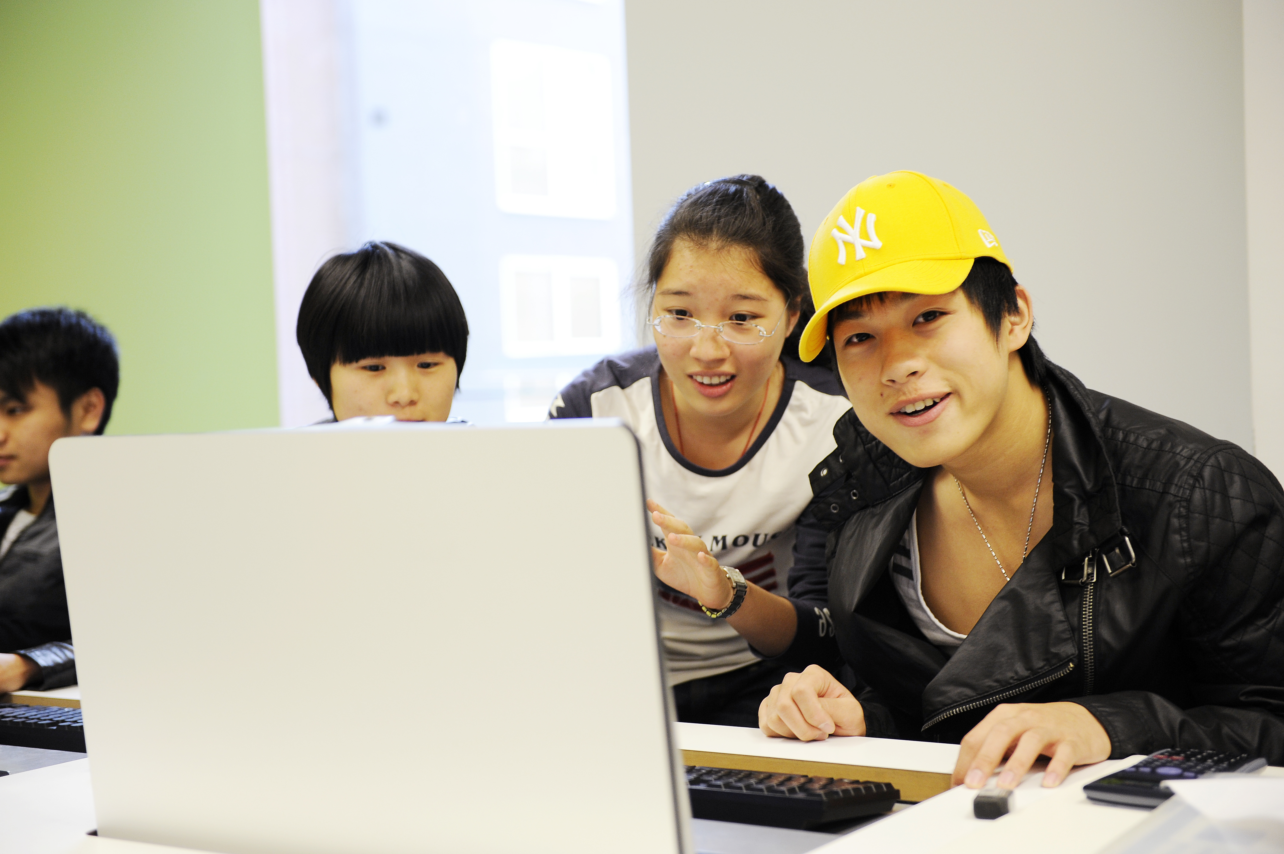 A group of three INTO International students are gathered around a desk-integrated computer