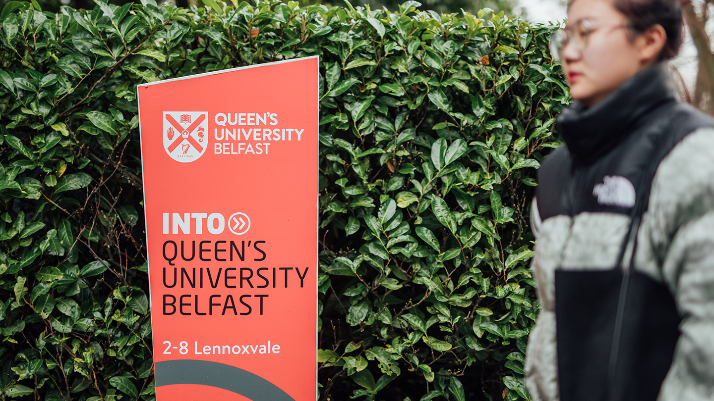 Student walking past Queen's University Belfast signpost 