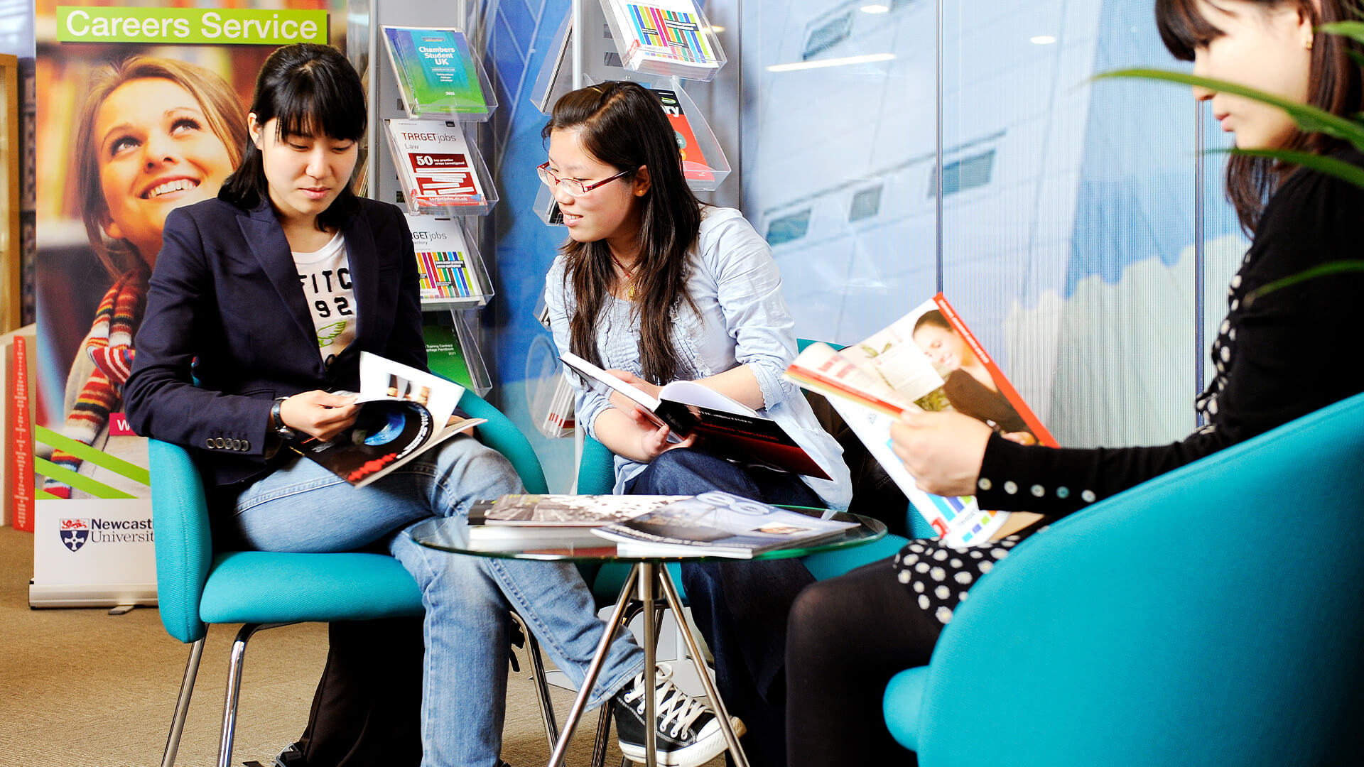 Students socialising and looking through publications in a breakout area on Newcastle University campus